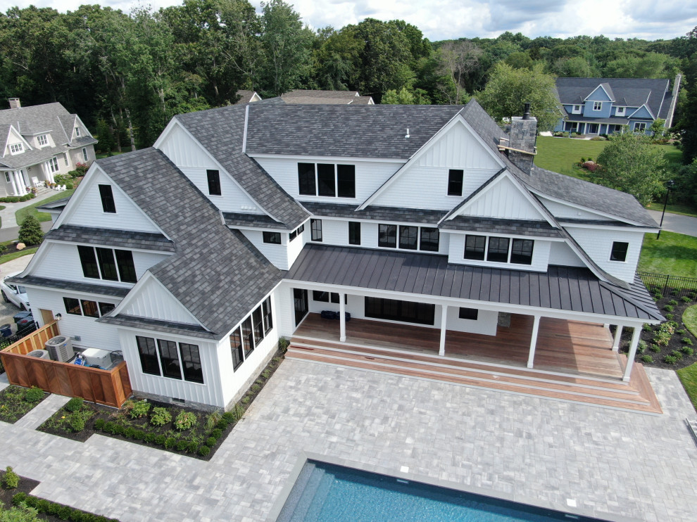 Cette image montre une très grande façade de maison blanche design en bois et planches et couvre-joints à deux étages et plus avec un toit à deux pans, un toit mixte et un toit noir.