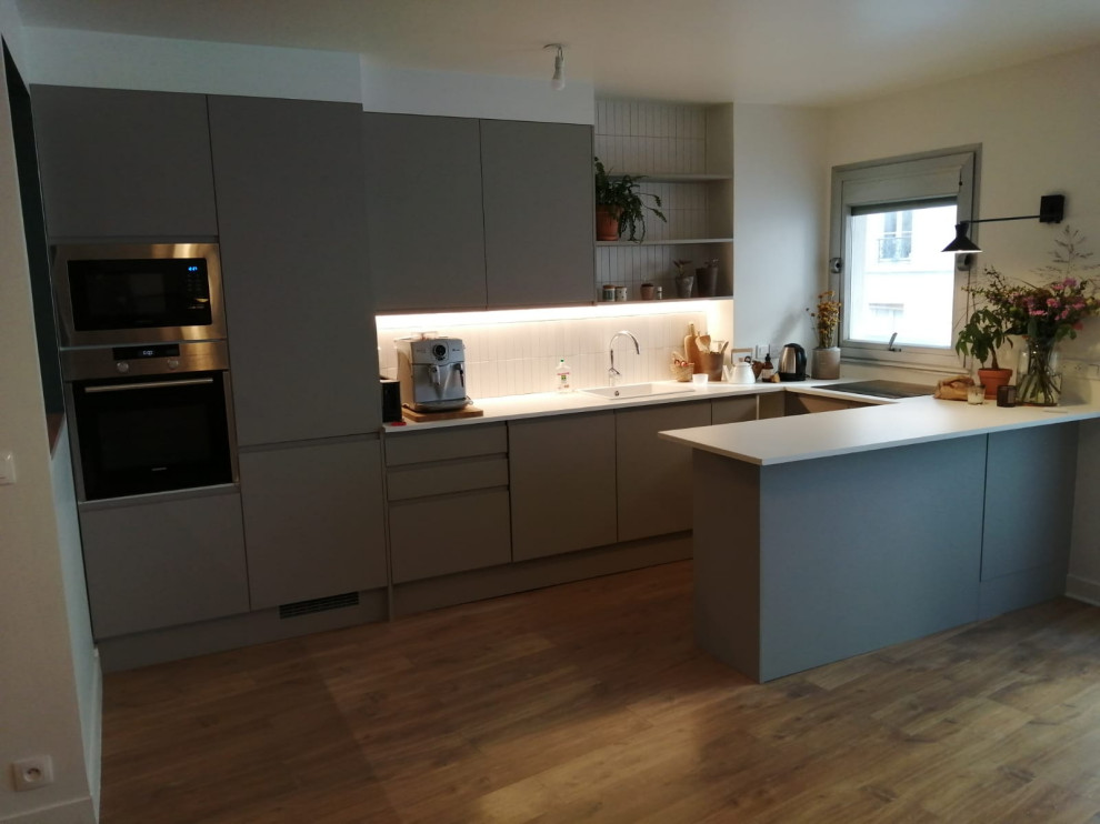 This is an example of a contemporary grey and white u-shaped kitchen/diner in Paris with a single-bowl sink, beaded cabinets, grey cabinets, wood worktops, white splashback, ceramic splashback, integrated appliances, laminate floors, an island, brown floors and white worktops.