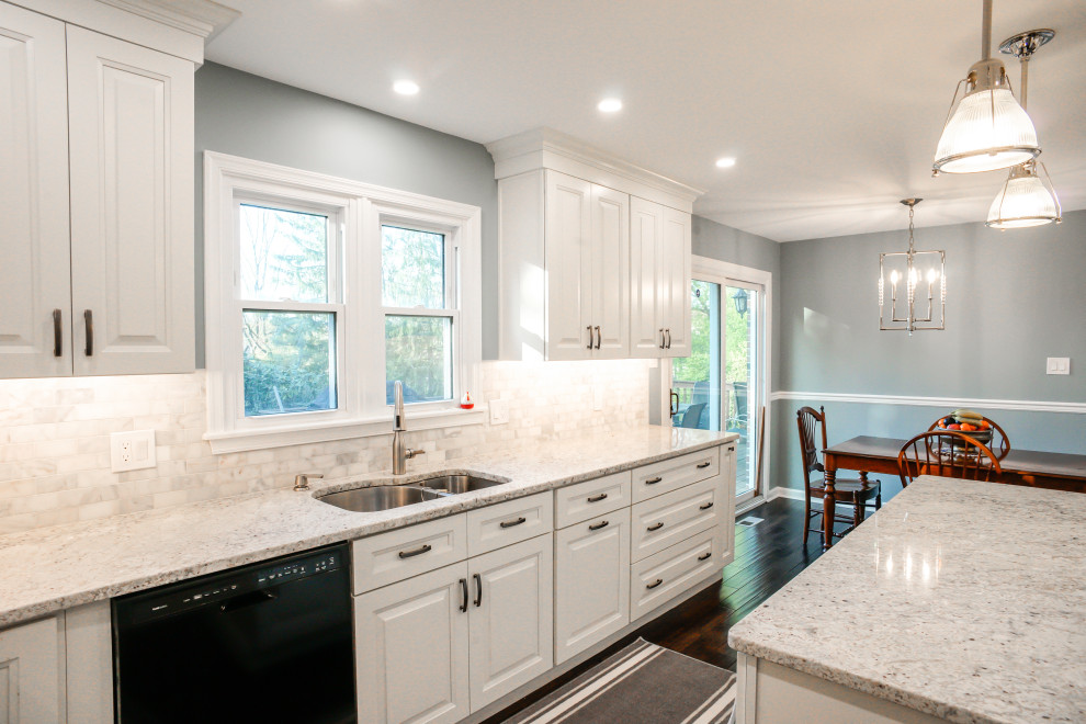 Inredning av ett klassiskt vit vitt kök, med en dubbel diskho, luckor med upphöjd panel, vita skåp, granitbänkskiva, grått stänkskydd, stänkskydd i marmor, mörkt trägolv, en köksö och brunt golv