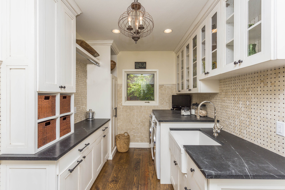 Large country galley utility room in Phoenix with a farmhouse sink, recessed-panel cabinets, white cabinets, soapstone benchtops, beige walls, medium hardwood floors, a side-by-side washer and dryer, brown floor and grey benchtop.