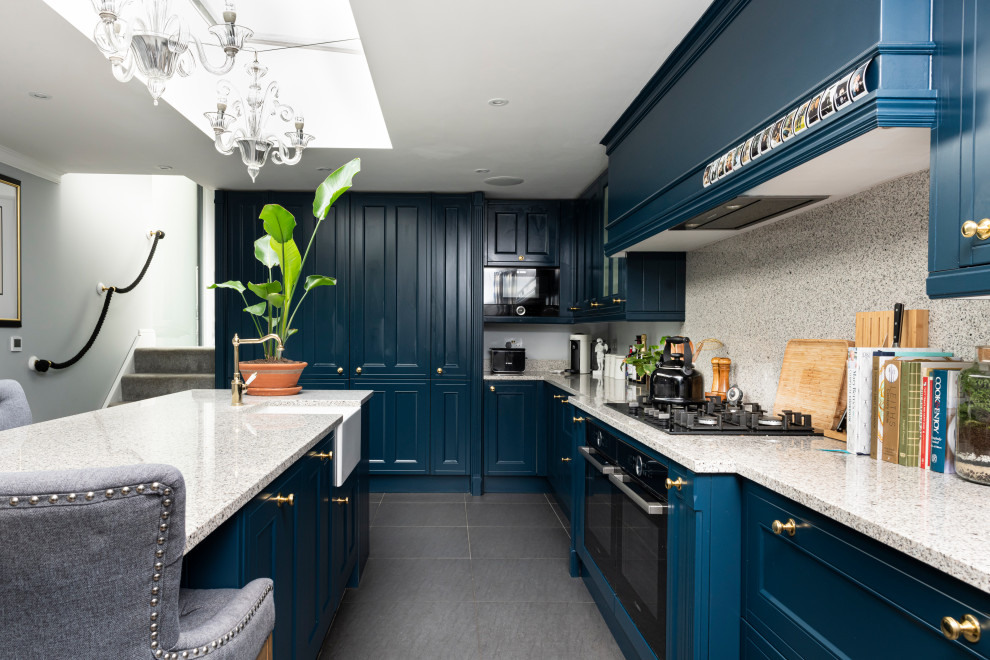 This is an example of a traditional kitchen/diner in London with blue cabinets, granite worktops, white splashback, granite splashback, an island, grey floors and white worktops.