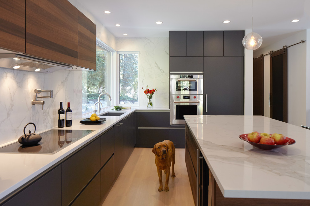 Photo of a large modern l-shaped eat-in kitchen in Seattle with panelled appliances, light hardwood floors, with island, an undermount sink, flat-panel cabinets, beige floor, black cabinets, solid surface benchtops, white splashback, porcelain splashback and white benchtop.