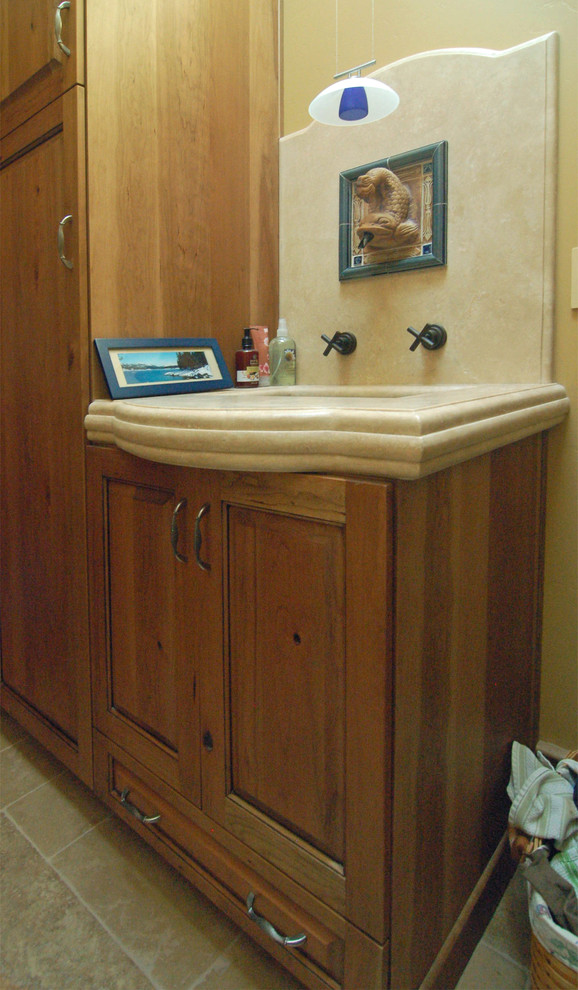 This is an example of a mid-sized transitional dedicated laundry room in San Luis Obispo with an undermount sink, raised-panel cabinets, limestone benchtops, yellow walls, travertine floors, a side-by-side washer and dryer and medium wood cabinets.