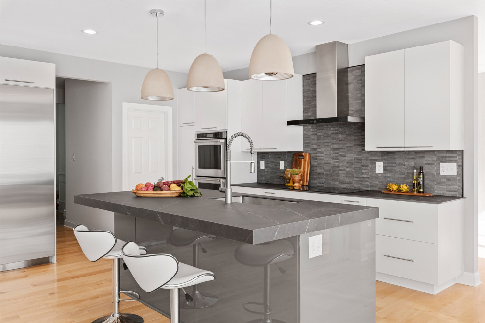 Large contemporary l-shaped kitchen/diner in DC Metro with a submerged sink, flat-panel cabinets, white cabinets, granite worktops, black splashback, ceramic splashback, stainless steel appliances, light hardwood flooring, an island and black worktops.