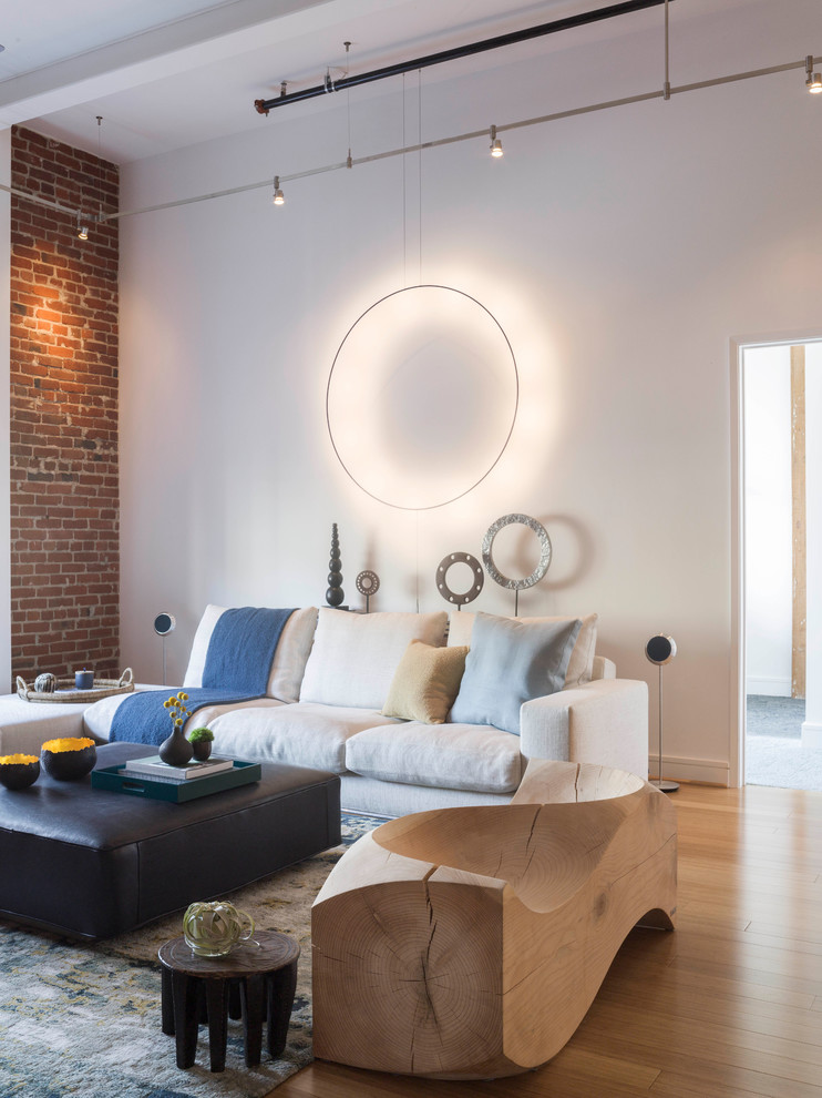 This is an example of a large industrial loft-style living room in San Francisco with white walls, light hardwood floors, brown floor and brick walls.