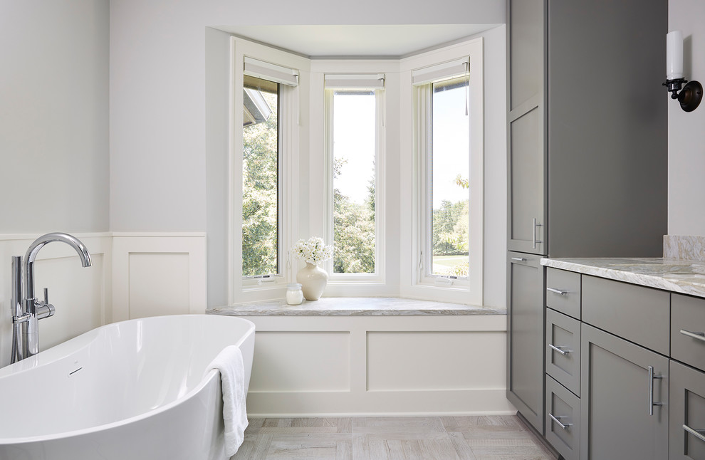 Design ideas for a large transitional master bathroom in Minneapolis with grey cabinets, a freestanding tub, grey walls, ceramic floors, granite benchtops, beige floor and shaker cabinets.