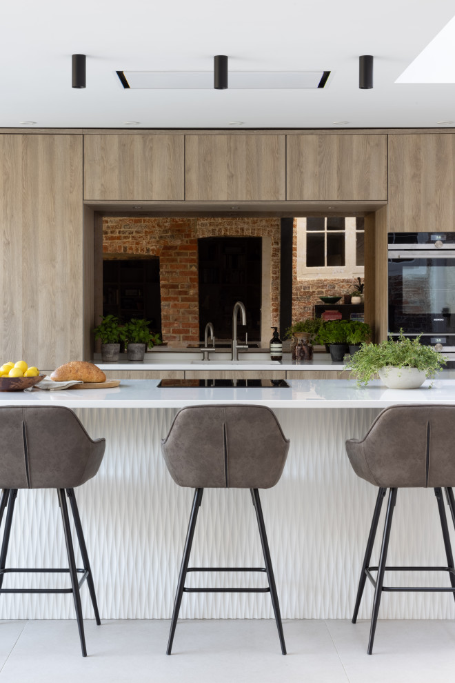 Inspiration for a mid-sized scandinavian eat-in kitchen in Hampshire with flat-panel cabinets, medium wood cabinets, solid surface benchtops, mirror splashback, black appliances, with island and white benchtop.