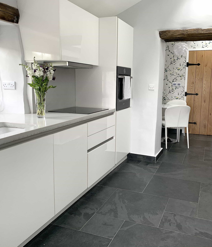 Inspiration for a mid-sized contemporary galley slate floor, black floor and exposed beam eat-in kitchen remodel with a single-bowl sink, flat-panel cabinets, white cabinets, concrete countertops, gray backsplash, cement tile backsplash, black appliances, no island and gray countertops