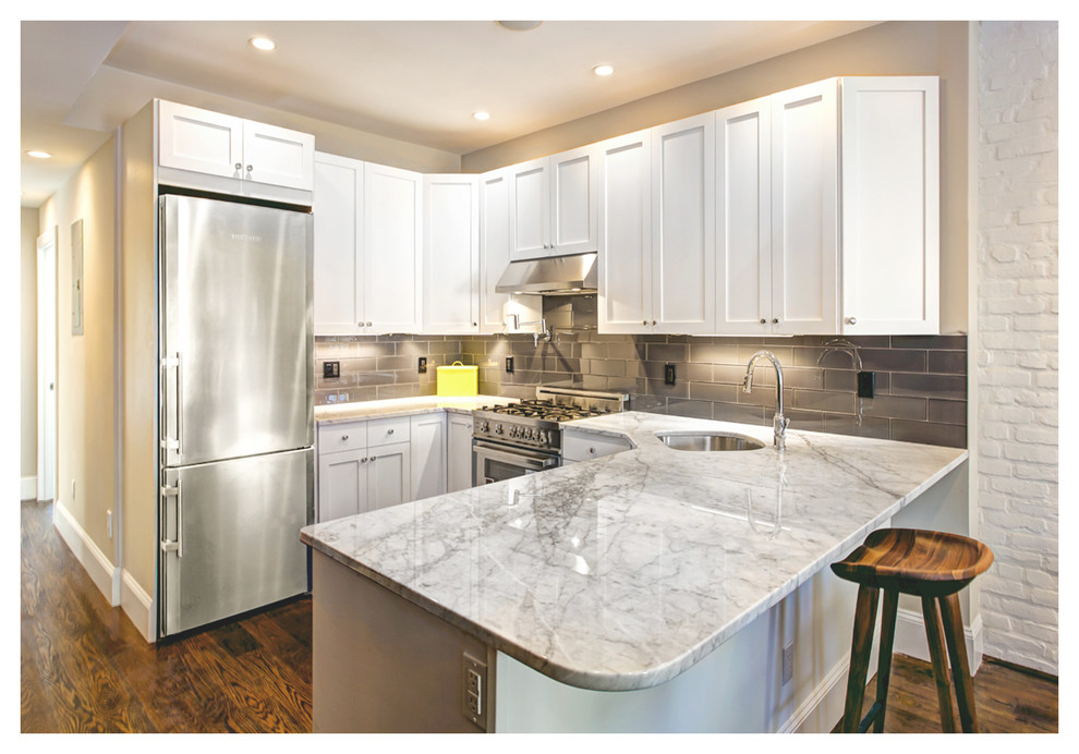 This is an example of a small traditional u-shaped kitchen in New York with an undermount sink, shaker cabinets, white cabinets, granite benchtops, grey splashback, subway tile splashback, stainless steel appliances, medium hardwood floors, a peninsula and brown floor.