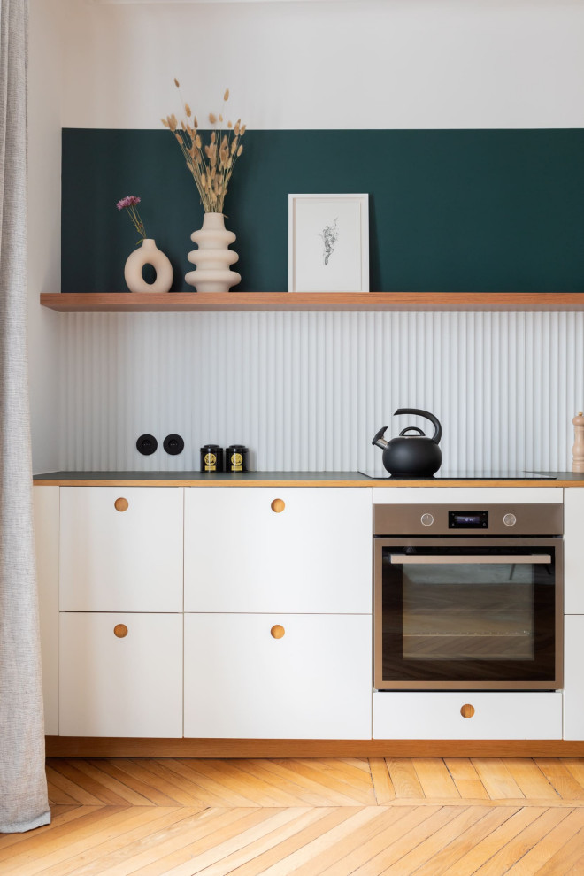 This is an example of a large scandi single-wall open plan kitchen in Paris with an integrated sink, light wood cabinets, white splashback, integrated appliances, medium hardwood flooring, no island and brown floors.