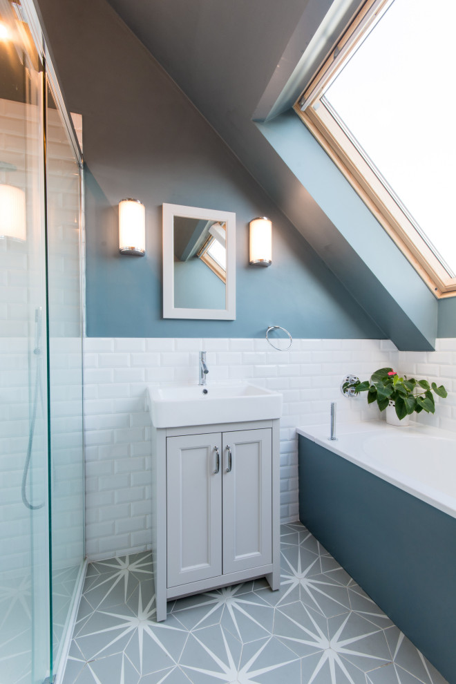 Inspiration for a transitional bathroom in London with recessed-panel cabinets, grey cabinets, an alcove tub, an alcove shower, white tile, subway tile, blue walls, a console sink and grey floor.
