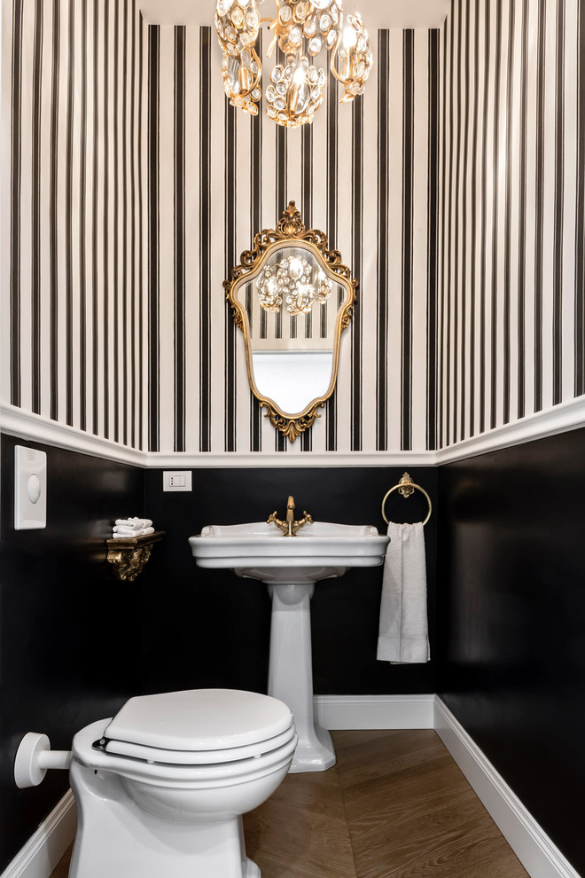 Photo of a small traditional powder room in Milan with a one-piece toilet, medium hardwood floors, a pedestal sink, brown floor and multi-coloured walls.