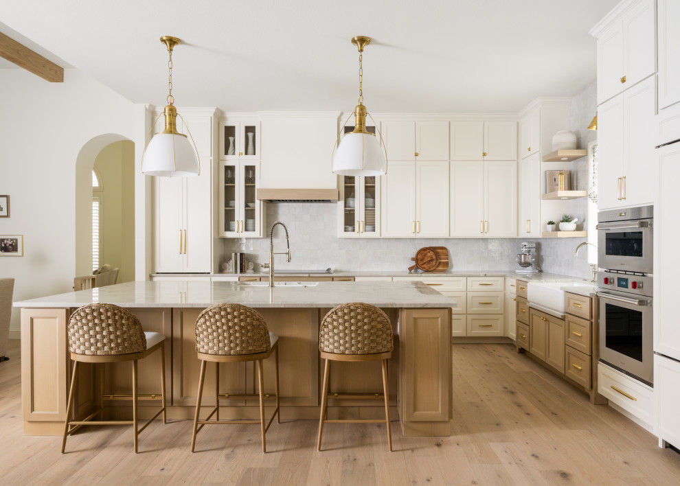 Mid-sized transitional l-shaped light wood floor and beige floor eat-in kitchen photo in Dallas with recessed-panel cabinets, light wood cabinets, quartzite countertops, white backsplash, ceramic backsplash, paneled appliances, an island, white countertops and an undermount sink