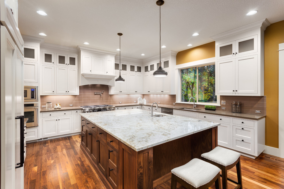 Large modern u-shaped kitchen in San Francisco with an undermount sink, shaker cabinets, white cabinets, quartz benchtops, pink splashback, glass tile splashback, stainless steel appliances, bamboo floors, with island, brown floor and grey benchtop.