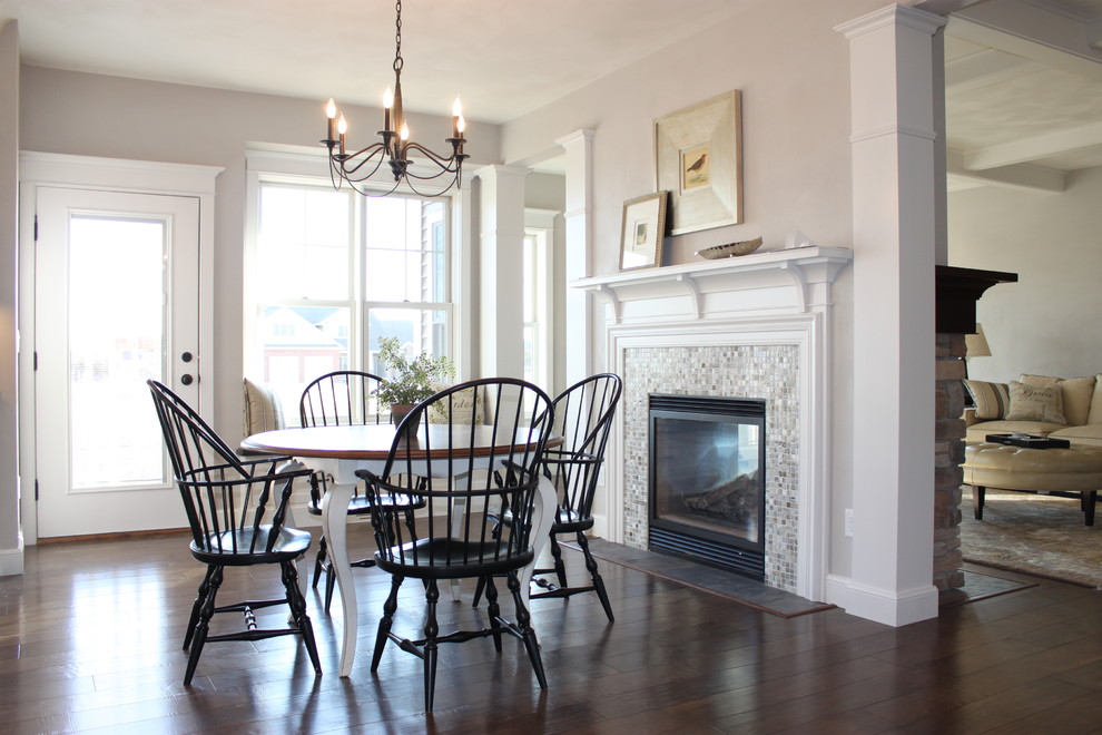 This is an example of a traditional dining room in Other with dark hardwood floors, a standard fireplace, a tile fireplace surround and beige walls.