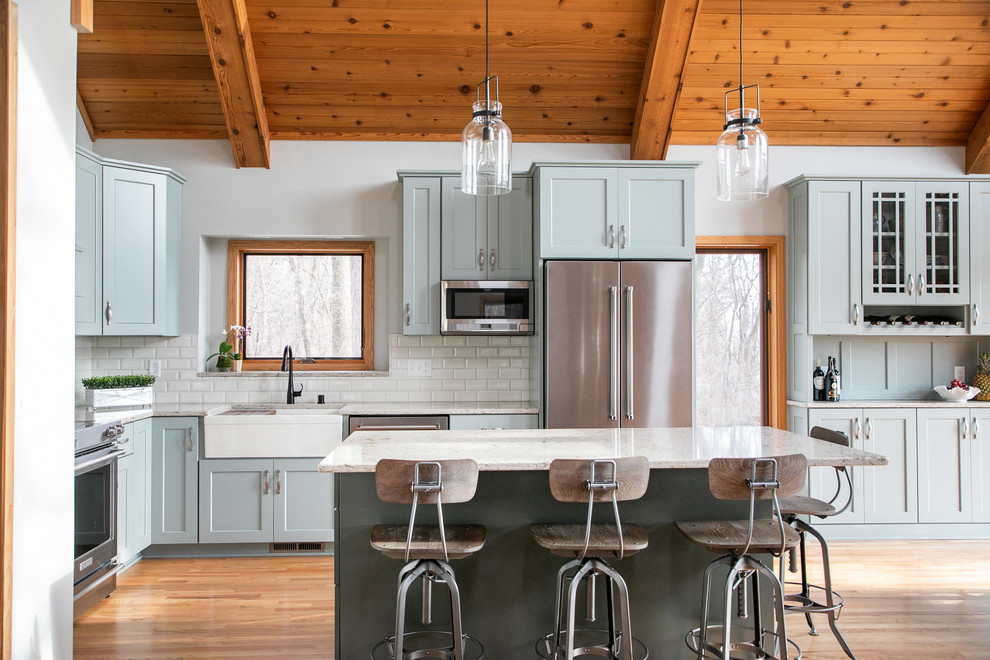 Inspiration for a country l-shaped kitchen in Other with a farmhouse sink, shaker cabinets, grey cabinets, white splashback, subway tile splashback, stainless steel appliances, medium hardwood floors, with island and white benchtop.