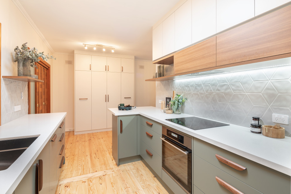 Foto på ett mellanstort funkis vit kök, med en undermonterad diskho, släta luckor, gröna skåp, bänkskiva i kvarts, grått stänkskydd, stänkskydd i porslinskakel, rostfria vitvaror, ljust trägolv och en halv köksö