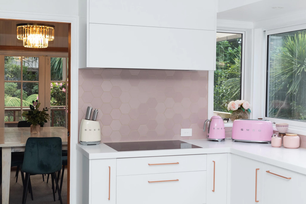 Стильный дизайн: п-образная кухня-гостиная среднего размера в стиле модернизм с врезной мойкой, плоскими фасадами, белыми фасадами, столешницей из акрилового камня, розовым фартуком, фартуком из керамической плитки, полом из керамической плитки и белой столешницей без острова - последний тренд