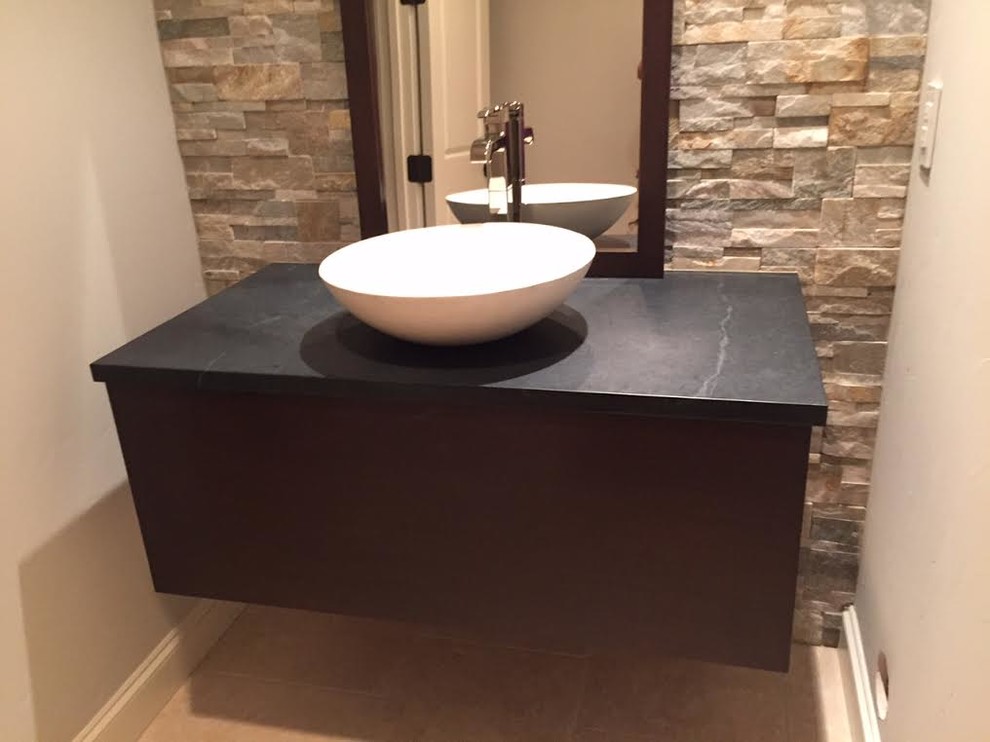 Inspiration for a small contemporary powder room in Dallas with flat-panel cabinets, black cabinets, beige walls, ceramic floors, a pedestal sink, beige tile, stone tile, soapstone benchtops and beige floor.