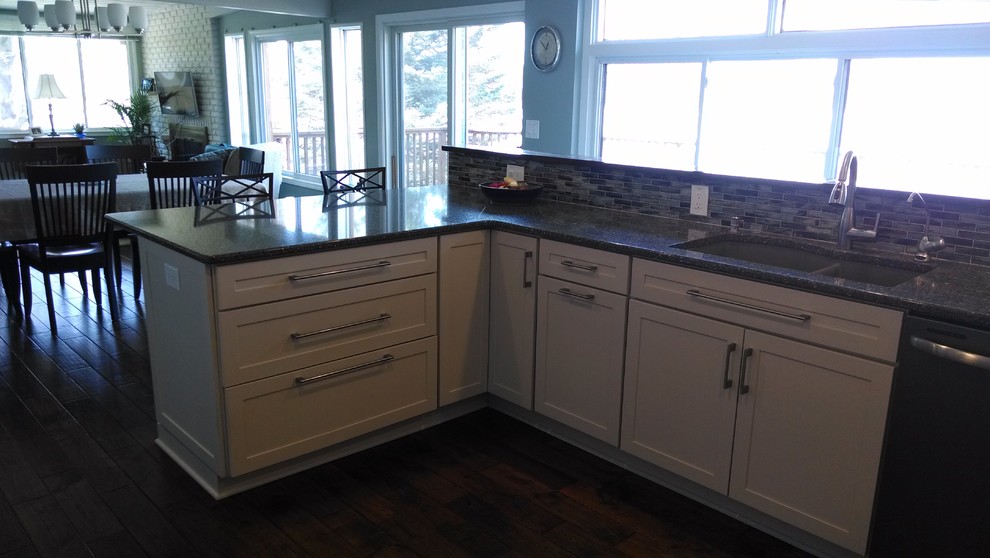 Example of a transitional dark wood floor eat-in kitchen design with an undermount sink, recessed-panel cabinets, white cabinets, quartz countertops, white backsplash, glass tile backsplash, stainless steel appliances and a peninsula