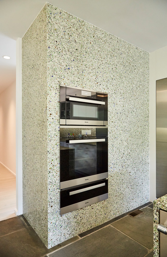 Mid-sized contemporary galley separate kitchen in New York with an undermount sink, flat-panel cabinets, white cabinets, recycled glass benchtops, green splashback, glass sheet splashback, stainless steel appliances, slate floors, with island and blue floor.