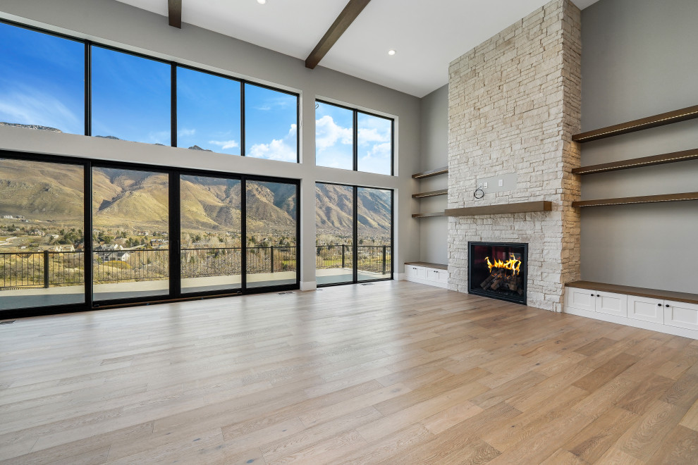 Photo of a large modern open plan games room in Salt Lake City with grey walls, medium hardwood flooring, a standard fireplace, a stacked stone fireplace surround, a wall mounted tv, brown floors, exposed beams and wood walls.