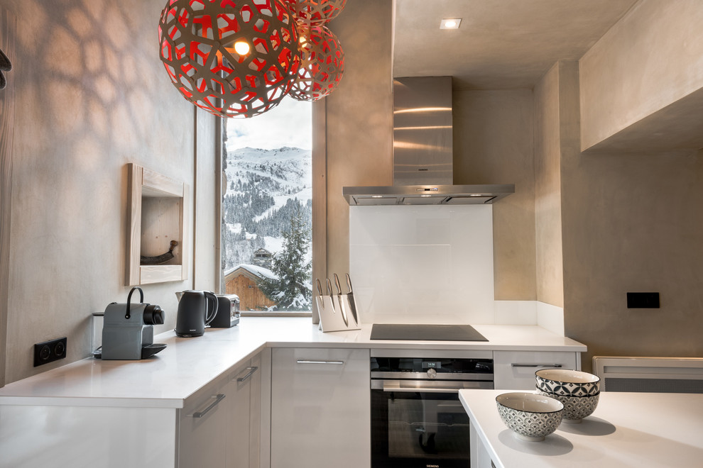 Exemple de cuisine in L With des portes de placard blanches, une crédence blanche, une crédence en feuille de verre, un électroménager en acier inoxydable and îlot.