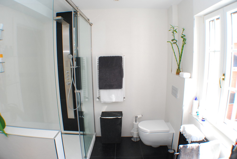 Imagen de cuarto de baño moderno con sanitario de pared, baldosas y/o azulejos blancas y negros, baldosas y/o azulejos de porcelana, paredes blancas, suelo de baldosas de porcelana, lavabo suspendido y encimera de acrílico