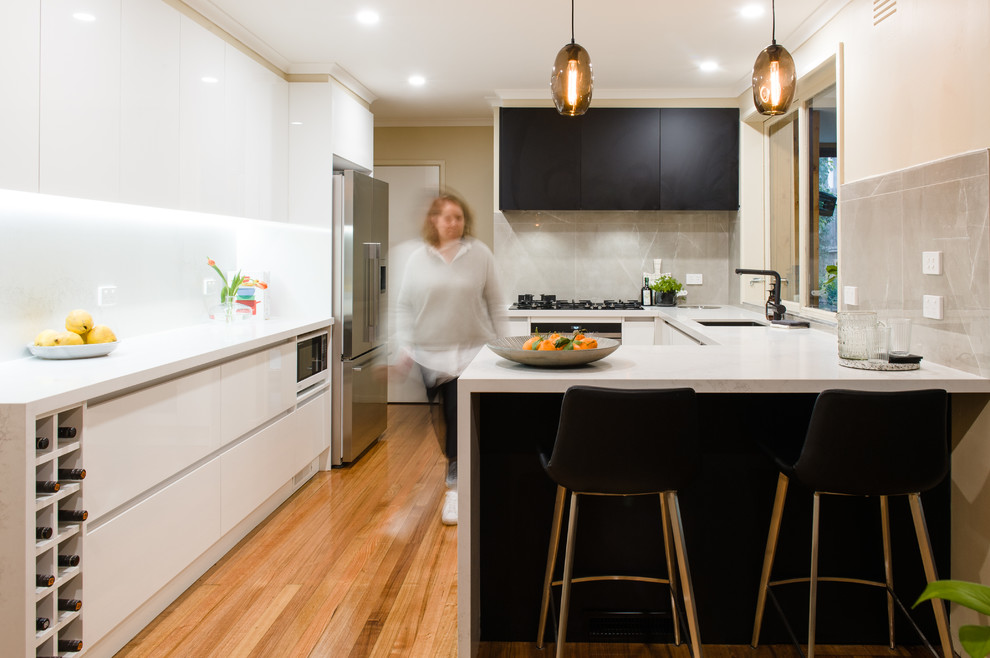 Mid-sized modern l-shaped kitchen pantry in Melbourne with an undermount sink, open cabinets, black cabinets, solid surface benchtops, mosaic tile splashback, stainless steel appliances, medium hardwood floors and with island.