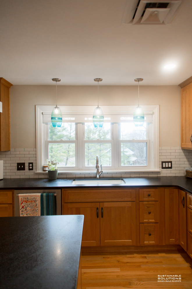 Example of a transitional kitchen design with shaker cabinets, medium tone wood cabinets, soapstone countertops, white backsplash, subway tile backsplash, stainless steel appliances, an island and black countertops