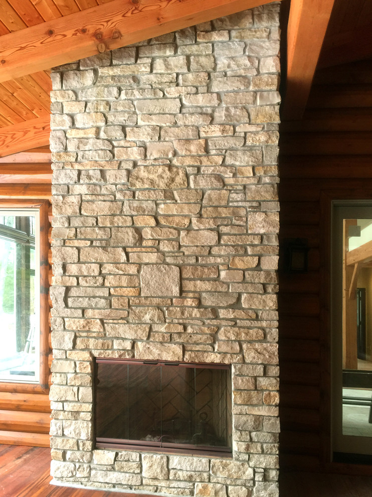 Large mountain style loft-style medium tone wood floor home design photo with a standard fireplace and a stone fireplace