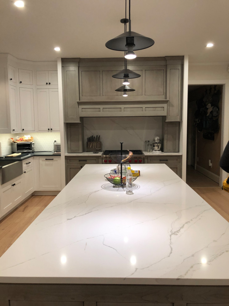 Inspiration for a large contemporary u-shaped open plan kitchen in New York with a farmhouse sink, beaded inset cabinets, white cabinets, quartz benchtops, white splashback, engineered quartz splashback, stainless steel appliances, light hardwood floors, with island, beige floor, white benchtop and vaulted.