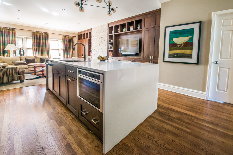 Mid-sized transitional u-shaped kitchen pantry in Chicago with an undermount sink, shaker cabinets, dark wood cabinets, solid surface benchtops, grey splashback, glass tile splashback, stainless steel appliances, medium hardwood floors and with island.