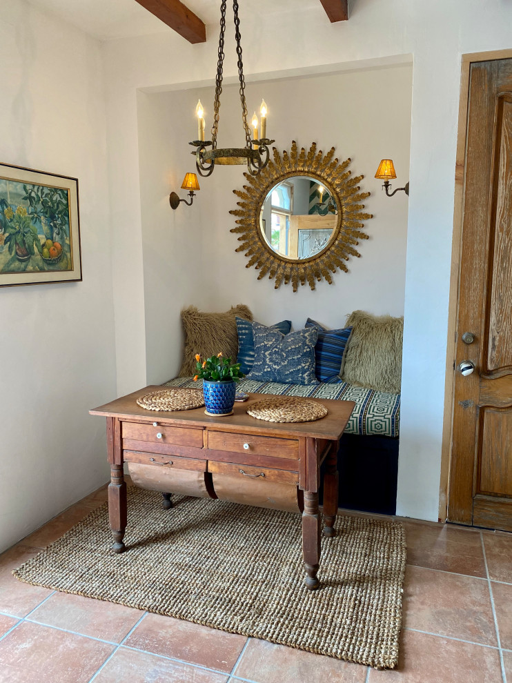 Inspiration for a small mediterranean dining room in San Diego with banquette seating, white walls, porcelain flooring, a corner fireplace, a plastered fireplace surround, orange floors, exposed beams and feature lighting.
