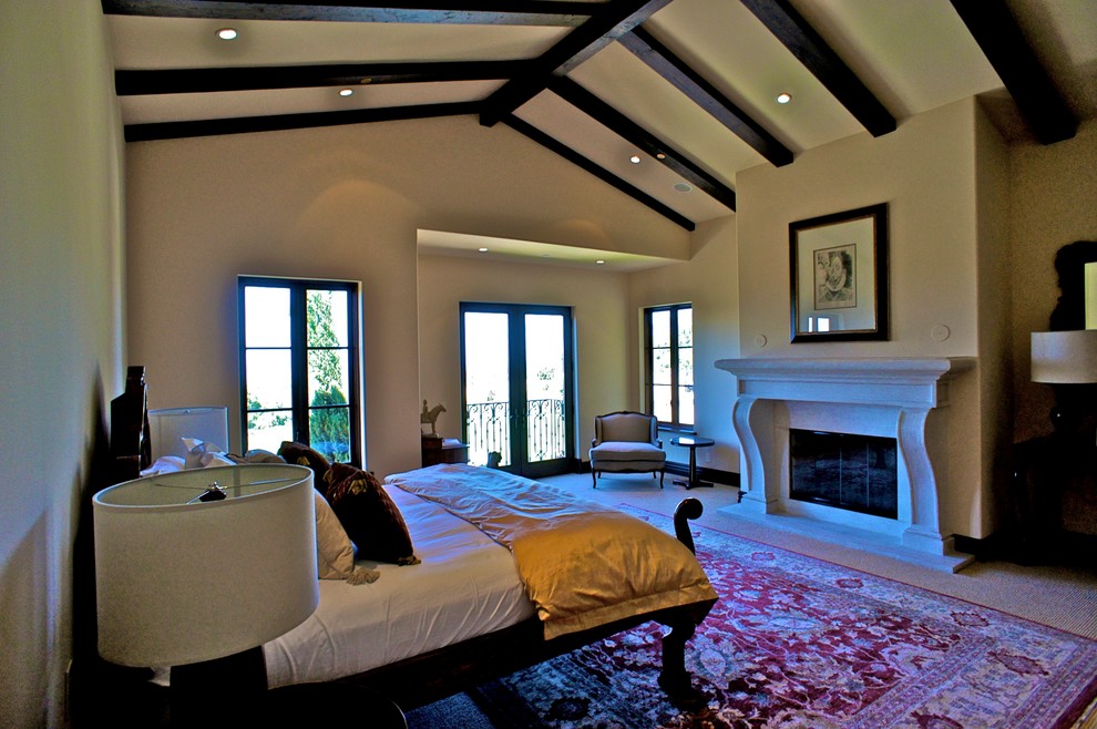 Large mediterranean loft-style bedroom in Santa Barbara with beige walls, carpet, a standard fireplace and a stone fireplace surround.