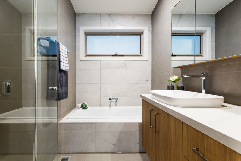 This is an example of a contemporary master bathroom in Melbourne with light wood cabinets, a drop-in tub, a corner shower, white tile, porcelain tile, grey walls, ceramic floors, a vessel sink and marble benchtops.
