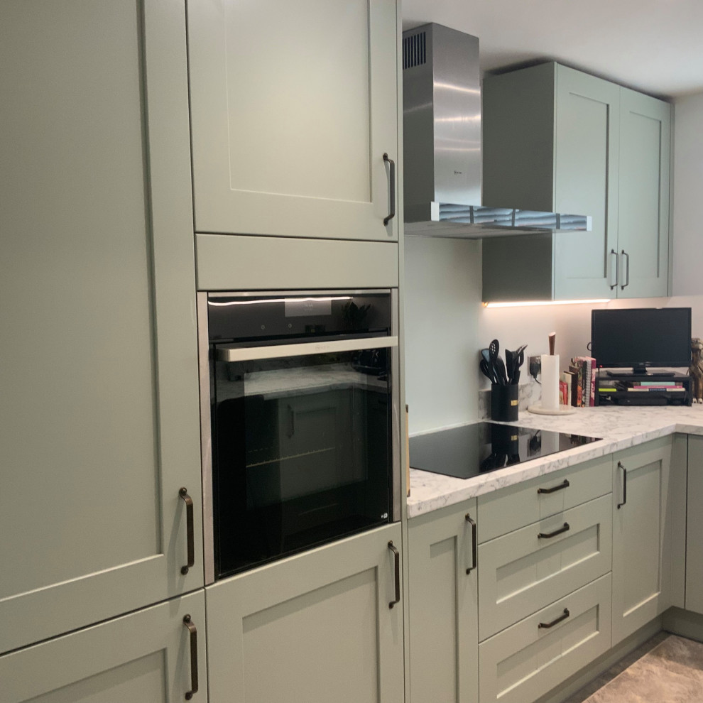 Inspiration for a mid-sized contemporary u-shaped gray floor enclosed kitchen remodel in Buckinghamshire with shaker cabinets, green cabinets, laminate countertops, white backsplash, glass sheet backsplash, paneled appliances, a peninsula and white countertops