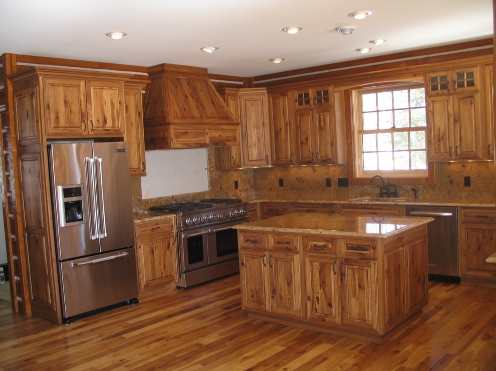 Design ideas for a mid-sized country l-shaped eat-in kitchen in New York with an undermount sink, raised-panel cabinets, dark wood cabinets, granite benchtops, beige splashback, stone slab splashback, stainless steel appliances, dark hardwood floors and with island.