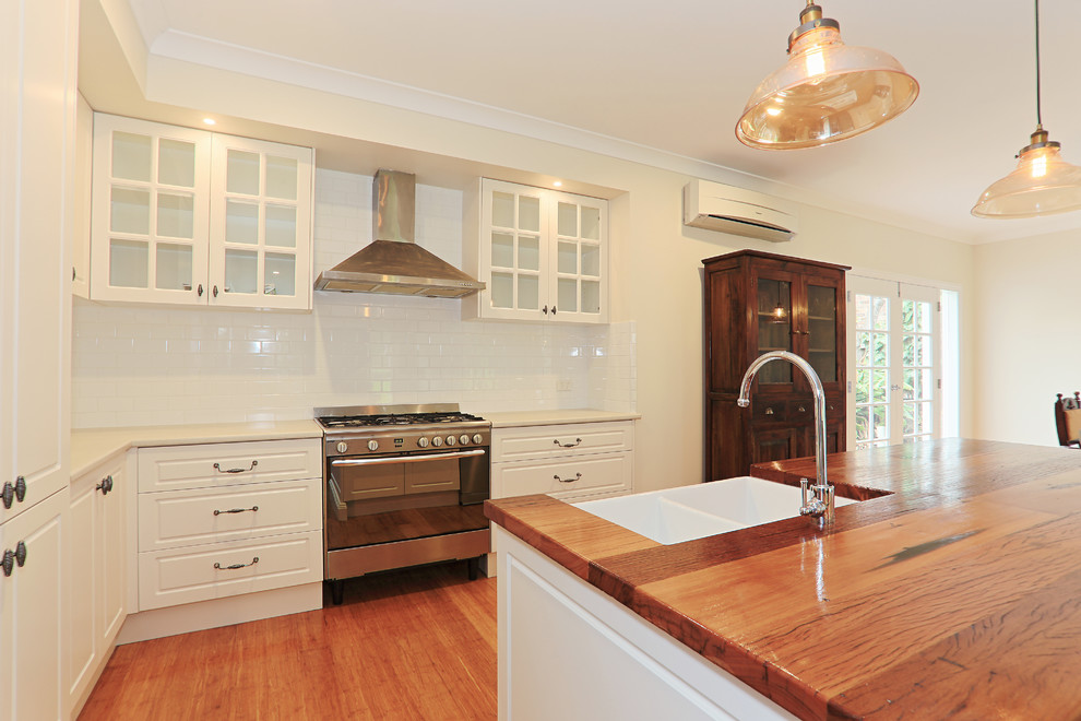Mid-sized traditional l-shaped eat-in kitchen in Melbourne with an undermount sink, recessed-panel cabinets, white cabinets, wood benchtops, white splashback, subway tile splashback, stainless steel appliances, medium hardwood floors and with island.