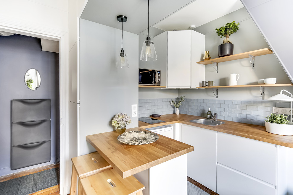 Photo of a mid-sized scandinavian u-shaped open plan kitchen in Paris with an undermount sink, flat-panel cabinets, white cabinets, wood benchtops, grey splashback, ceramic splashback, stainless steel appliances, light hardwood floors, no island, brown floor and brown benchtop.