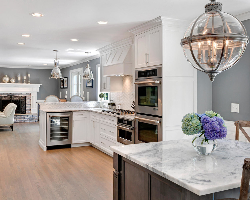 Inspiration for a large transitional l-shaped separate kitchen in New York with a farmhouse sink, recessed-panel cabinets, grey cabinets, marble benchtops, white splashback, stone tile splashback, stainless steel appliances, light hardwood floors and with island.