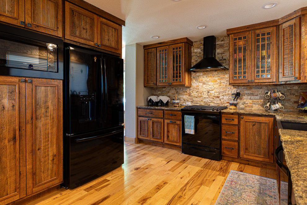 Inspiration for a mid-sized rustic l-shaped light wood floor and brown floor eat-in kitchen remodel in Denver with a farmhouse sink, raised-panel cabinets, medium tone wood cabinets, granite countertops, multicolored backsplash, stone tile backsplash, black appliances, no island and beige countertops
