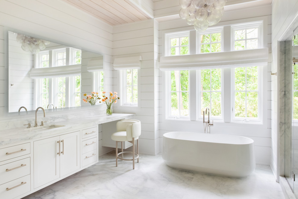 На фото: огромная главная ванная комната, совмещенная с туалетом в стиле неоклассика (современная классика) с белыми фасадами, отдельно стоящей ванной, душем в нише, белыми стенами, мраморным полом, монолитной раковиной, мраморной столешницей, белым полом, душем с распашными дверями, белой столешницей, тумбой под две раковины, встроенной тумбой, сводчатым потолком, панелями на части стены и фасадами в стиле шейкер