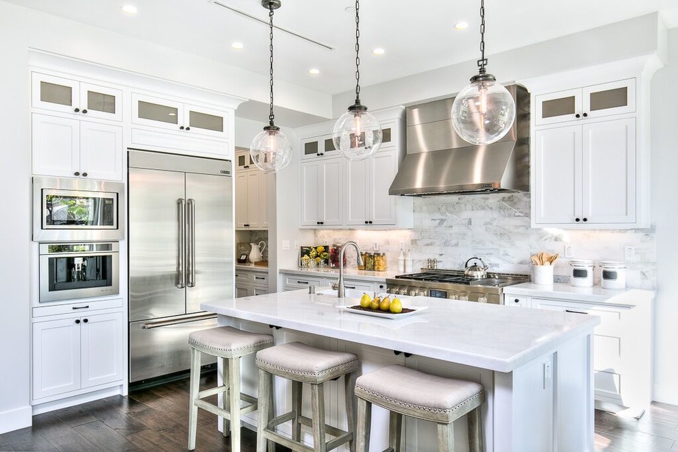Design ideas for a large transitional l-shaped eat-in kitchen in Orange County with shaker cabinets, white cabinets, white splashback, marble splashback, stainless steel appliances, dark hardwood floors, with island, brown floor, a farmhouse sink and marble benchtops.