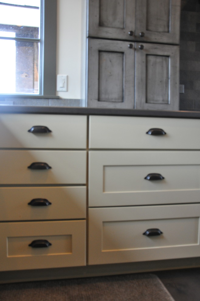 Inspiration for a large rustic l-shaped medium tone wood floor eat-in kitchen remodel in Seattle with an undermount sink, shaker cabinets, distressed cabinets, quartz countertops, gray backsplash, stone tile backsplash, stainless steel appliances and an island