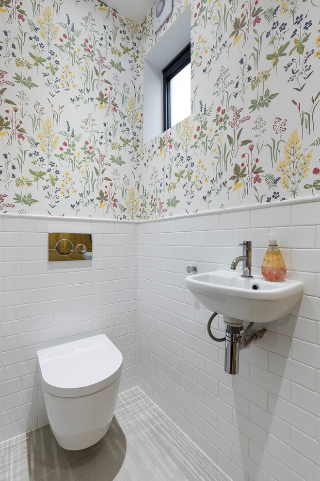 Photo of a transitional powder room in London with a wall-mount toilet, multi-coloured walls, a wall-mount sink and white floor.