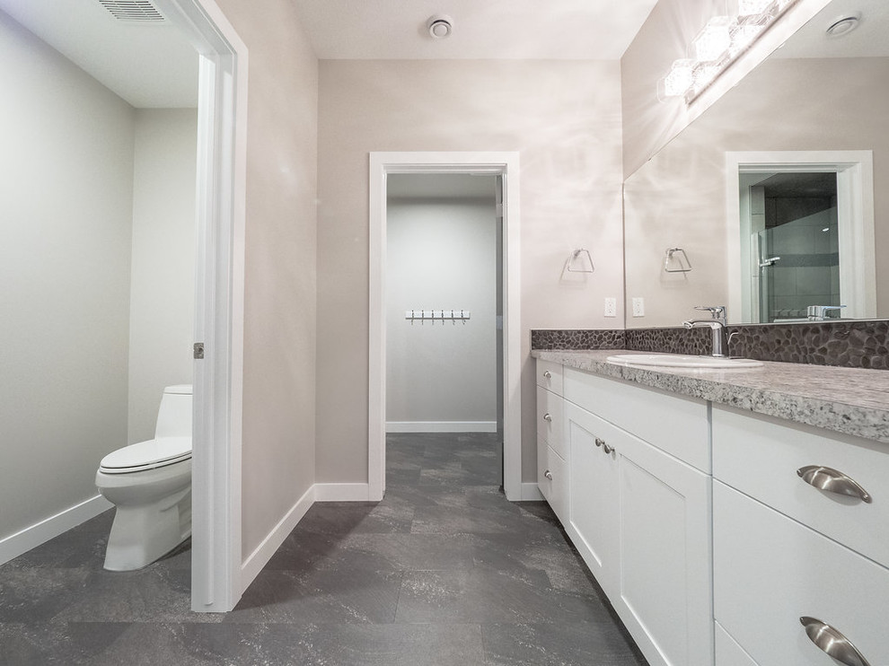 This is an example of a mid-sized traditional 3/4 bathroom in Edmonton with flat-panel cabinets, white cabinets, a double shower, a two-piece toilet, black tile, grey walls, vinyl floors, a drop-in sink, laminate benchtops, grey floor, a sliding shower screen and pebble tile.