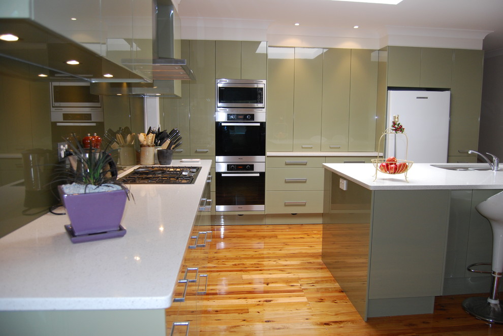 Inspiration for a large modern l-shaped eat-in kitchen in Sydney with an undermount sink, flat-panel cabinets, green cabinets, quartz benchtops, green splashback, glass sheet splashback, stainless steel appliances, medium hardwood floors and with island.