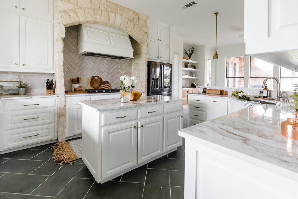 Inspiration for a beach style u-shaped kitchen in Dallas with an undermount sink, raised-panel cabinets, white cabinets, beige splashback, subway tile splashback, black appliances, with island, grey floor and multi-coloured benchtop.