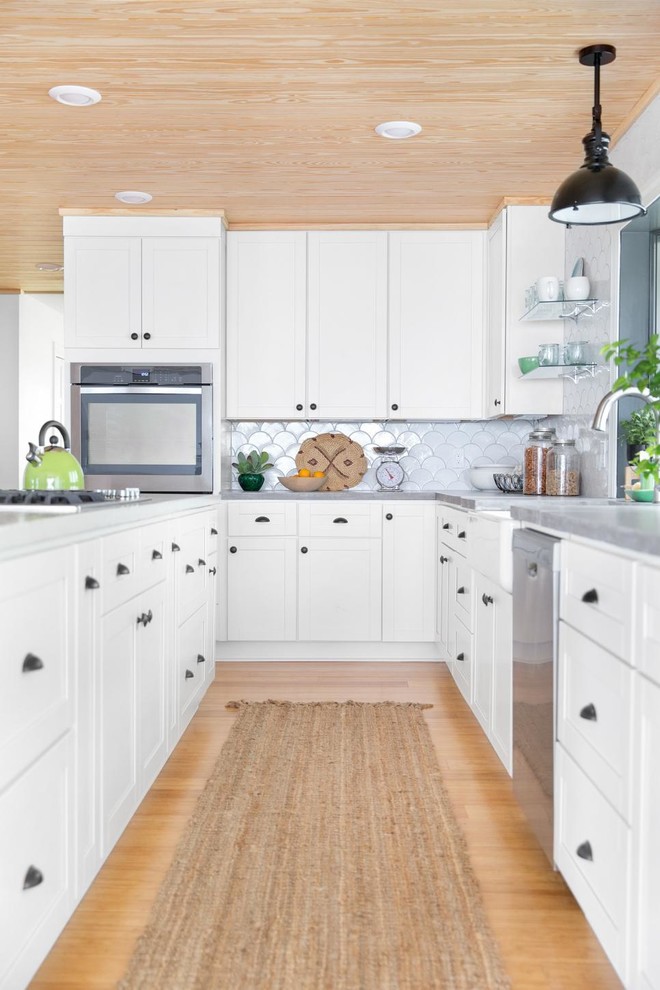 Design ideas for a transitional l-shaped kitchen in Orlando with a farmhouse sink, shaker cabinets, white splashback, ceramic splashback, stainless steel appliances, bamboo floors, white cabinets, with island and concrete benchtops.